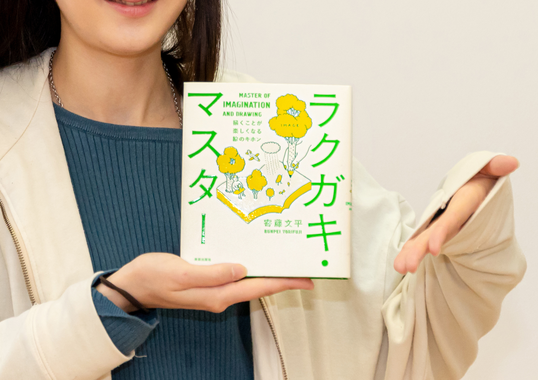落書きマスターという本を指さすカズミアの女性スタッフ